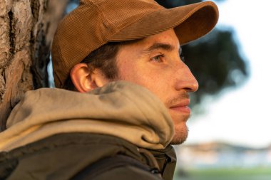 Parkta bir ağaca yaslanan bir adam şehrin günbatımını ve sonbahar renklerini düşünür.