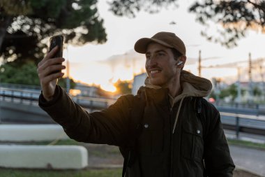 Bir adam öğleden sonra şehirde yürürken selfie çeker.
