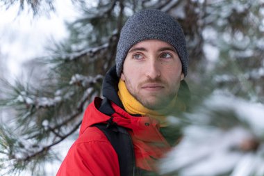 Genç yakışıklı beyaz adam kış mevsiminde dağ ormanlarında yürüyüş yapıyor. Spor macera yaşam tarzı. Karlı bir arazide yolculuk