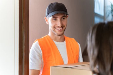 Teslimatçı eve paket getiriyor. Gülümseyen taşıyıcı bir karton kutu yolluyor.