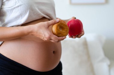 Hamile bir kadın donuttan şeker mi yoksa sağlıklı bir meyve mi yiyeceğine karar veriyor.