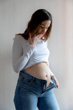 Karnı şişmiş bir kadın yüzünden pantolonunu ilikleyemeyen bir kadın.