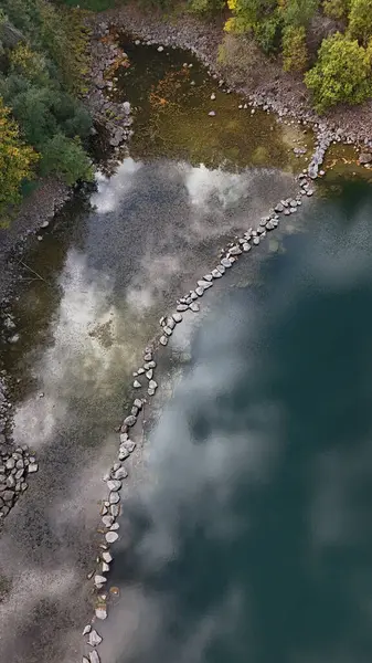 Ormanda taşları olan küçük bir gölün etrafındaki renkli sonbahar ağaçlarının havadan görünüşü