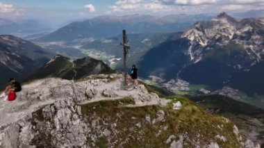 İnsanlar bir dağın tepesinde oturuyorlar. Arkasında dağlar ve vadiler var. Yörüngesel dron videosu. Hoher Burgstall, Yedi Zirve Stubai, Tirol, Avusturya..