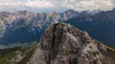 İnsanlar bir dağın tepesinde oturuyorlar. Arkasında dağlar ve vadiler var. Yörüngesel dron videosu. Hoher Burgstall, Yedi Zirve Stubai, Tirol, Avusturya..