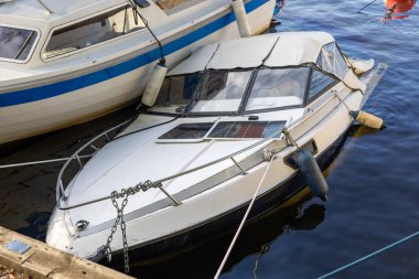 Bir iskeleye bağlı, kısmen suya batmış beyaz bir tekne. Teknenin tepesinde bir gölgelik ve su yüzeyinde yansımaları olan bir güneş paneli var..