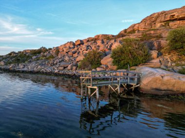 Batan güneşin arka plandaki kırmızı graniti parlatmasıyla eğri, eski bir iskelenin havadan yakından görüntüsü..