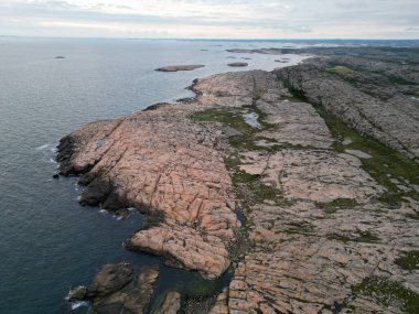 Denizin üzerinde güneşin batışının ve İsveç 'in Bohuslan kentindeki kırmızı granit kayalara yansımasının havadan çekilmiş fotoğrafı..