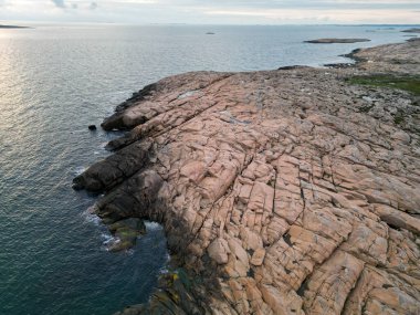 Sahilde görünen çatlaklar ve yeşillik parçalarıyla engebeli kayalık arazinin havadan görünüşü. Manzara, bir su kütlesine bitişik pürüzsüz ve pürüzsüz kaya oluşumlarının bir karışımını içerir..