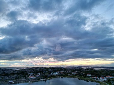 A scenic view of a cloudy sky over a tranquil sea, with islands visible in the foreground. The clouds are dramatic, casting shadows on the water, while the horizon glows with soft pastel colors from the sunset. clipart