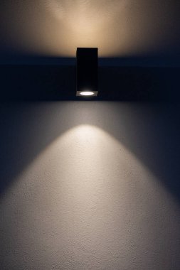 A wall light shines on a wall during evening hours, casting a long light. clipart