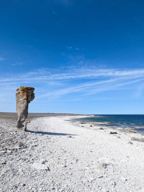 Çakıl dolu bir sahil boyunca eşsiz kaya oluşumlarının yer aldığı sakin bir kıyı manzarası. Açık mavi gökyüzü sakin denizle çelişiyor ve barışçıl bir atmosfer yaratıyor..
