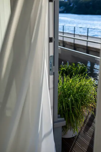 Saksı bitkisi açık bir balkon kapısından görülebilir. Rıhtımın yanında, rüzgar beyaz perdeyi uçururken..