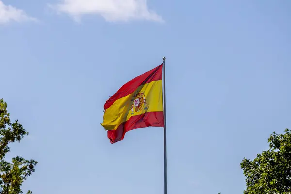 stock image A vibrant Spanish flag waving against a clear blue sky, on the Spanish embassy in Stockholm, Sweden. Surrounded by green trees.