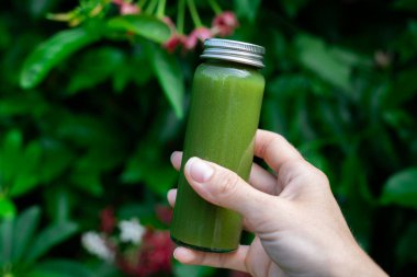 Canlı tropikal yaprakların önünde elinde yeşil detoks suyu şişesi tutuyordu. Sağlıklı yaşam tarzı ve egzotik orman geçmişi üzerine organik beslenme konsepti. Sağlık ve doğal beslenme konsepti.
