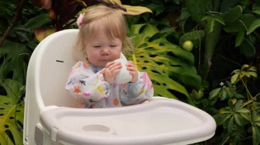 Tatlı çocuk, yemyeşil bir tropikal bahçede plastik bir sandalyeye oturmayı öğreniyor, erken çocukluk dönüm noktası, bebek bağımsızlığı, olağanüstü bir bebek, yemyeşil bir tropik bahçede plastik bir sandalyeye oturmayı öğreniyor.