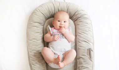 Bebek yuvasında ayaklarıyla oynayan beyaz, şirin bir kız bebek. bebek dönüm noktaları