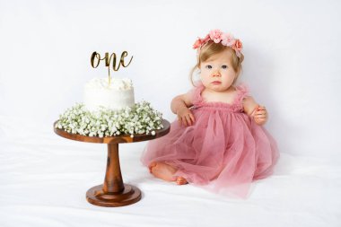 Beyaz, tatlı bir bebek ilk doğum gününde pastasına bakıyor. Küçük kız doğum günü pastası. Bir yıllık doğum günü kutlaması. Bebek gibi düşün. İlk pasta.. 