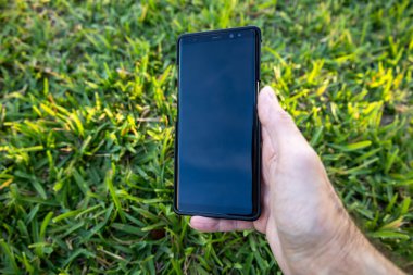 Erkekler el ele tutuşup yeşil çimlerin arkasında siyah telefon tutarlar.