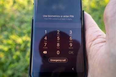 Erkekler siyah telefondan yeşil çimen arka bahçesine şifre girerler.