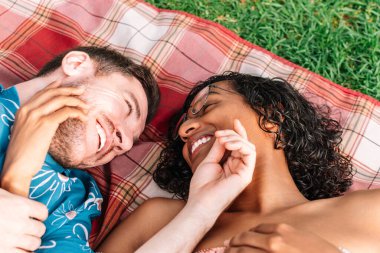 A transgender woman and a man are lying on a blanket in a park, smiling and laughing together. The scene is lighthearted and carefree, as the couple enjoys each other's company in a relaxed atmosphere clipart