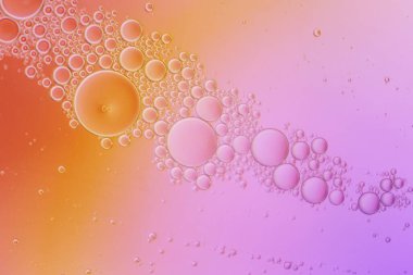 Bir yağ ve su karışımının makro fotoğrafçılığı pembe turuncu arka planda kabarcıklar oluşturur.