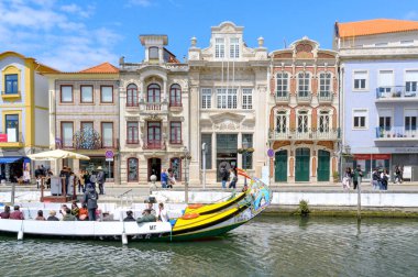 Tourists ride colorful traditional boat barcos moliceiros along canals Ria de Aveiro, Portugal. Canals bordered colorful historic Art Nouveau buildings.