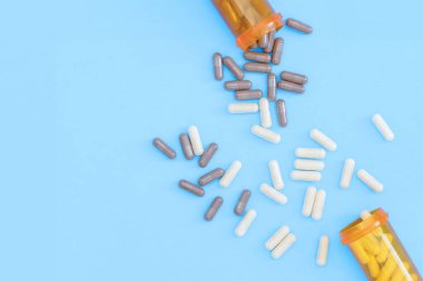 Rastgele dağılmış beyaz ve kahverengi ilaç kapsüllerinin düz bir fotoğrafı ve mavi arka planda iki hap kutusu vardı. Kopyalamak için boşluk.