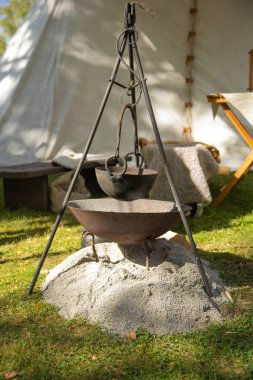 Bir taşın arkasındaki çadırda büyük bir demir çaydanlık ateşin üzerinde duruyor.