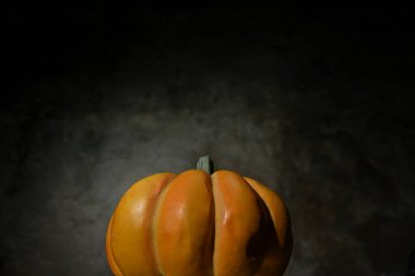 Canlı bir turuncu balkabağı ön planda belirgin bir şekilde koyu ve sessiz bir arkaplanda duruyor. Normalde cadılar bayramı festivali için sembolik olarak kullanılır..