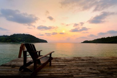 Ahşap sandalye, sahil evinin balkonunda günbatımı arka planında oturur.