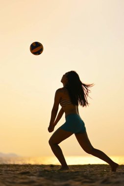 Gün batımında plaj voleybolunda kadın silueti topa vuruyor..