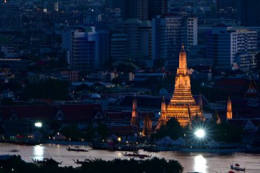 Geceleyin Antik Wat Arun 'un altın ışıklarıyla, arka planda mavi gölge ve modern yaşam tarzı çok kotrast. Nehirde kraliyet mavnası alayı da var..