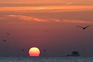 Silhouette of the fisherman's bamboo hut(kra teng) during the sunrise over the sea. Before completely float over the sea,the sun's shape is similar to the shape of Omega sign. clipart