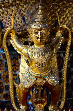 Close up of Garuda statue subduing the Naga, stucco covered with gold leaf, decorating around the ordination hall of Wat Phra Sri Rattana Satsadaram. clipart