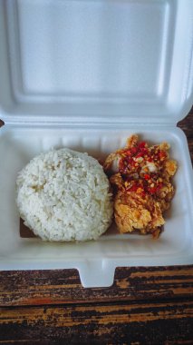 İçinde tavuk ve biber sosu bulunan geprek pilavı dolu bir yemek kutusu.