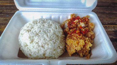 İçinde tavuk ve biber sosu bulunan geprek pilavı dolu bir yemek kutusu.