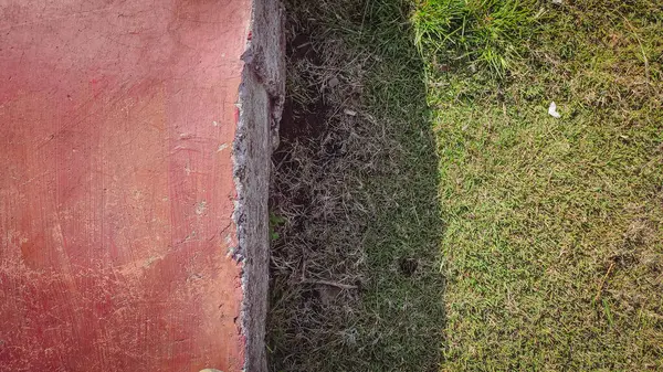 Kırmızı çimento, yanında gölgesi olan yeşil çimenler var.