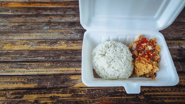 İçinde tavuk ve biber sosu bulunan geprek pilavı dolu bir yemek kutusu.