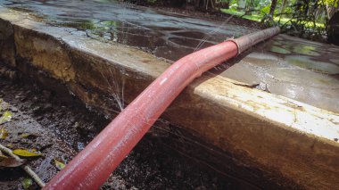 Uzun kırmızı bir hortum sızdırıyor, böylece ıslanıyor ve su fışkırıyor.