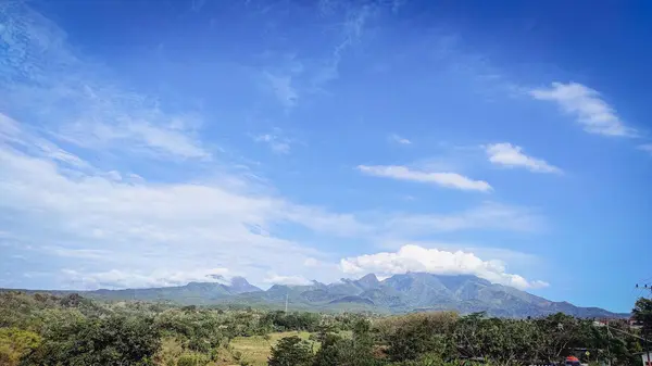 Çok bulutlu güzel bir dağ manzarası ve ayrıca açık mavi gökyüzü ve pirinç tarlalarının altında bazı yeşil bitkiler.