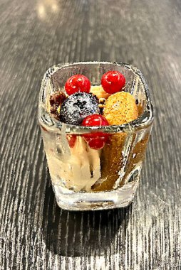 Şeffaf cam bir kapta böğürtlenlerle süslenmiş tatlı.