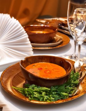 Kahverengi seramik kasede domates çorbası, servis edilen masada maydanozun yanında.