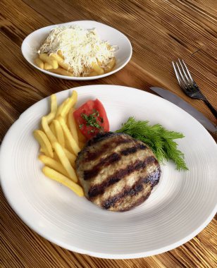 Kızarmış pirzola, patates kızartması ve ahşap bir yüzey üzerinde otlar.