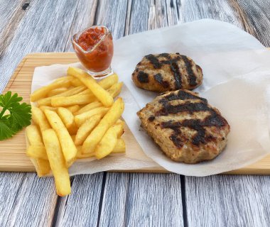 Kızarmış pirzola, patates kızartması ve ahşap bir yüzey üzerinde otlar.