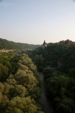 Yeşil tepelerin arka planında siyah çatıları ve mavi gökyüzünün altında bir nehri olan ortaçağ taş şatosu. Tarihsel mimari ve doğa resimsel bir görünüm yaratır..