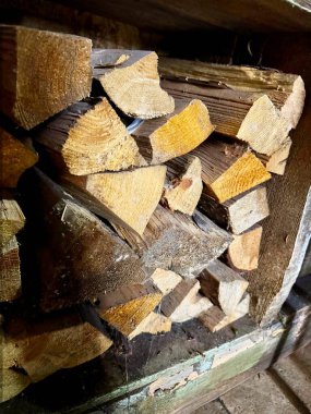 Fotoğrafta tahta bir kutuda kesilmiş odun yığını görülüyor. Tahtanın dokusu ve doğal çatlaklar görülebilir. Işıklandırma koyu ve açık renkler arasında bir kontrastlık yaratır..