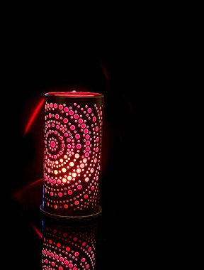 Mumların sıcak ışığının içinden geçtiği desenli delikleri olan bir lamba. Siyah arkaplan kontrastı vurguluyor ve rahatlık ve rahatlık ortamı yaratıyor..