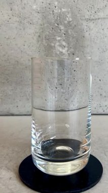 Şeffaf su, gri arka planda bir şişeden bir bardağa dökülür. Minimalist tarz, temiz içme suyu konsepti ve sağlıklı yaşam tarzı..