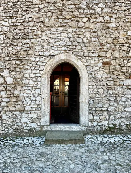 Tarihi bir binanın taş duvarındaki eski ahşap kapı. Ortaçağ tarzının mimar elementi ayaklarının altında kaldırım taşlarıyla.